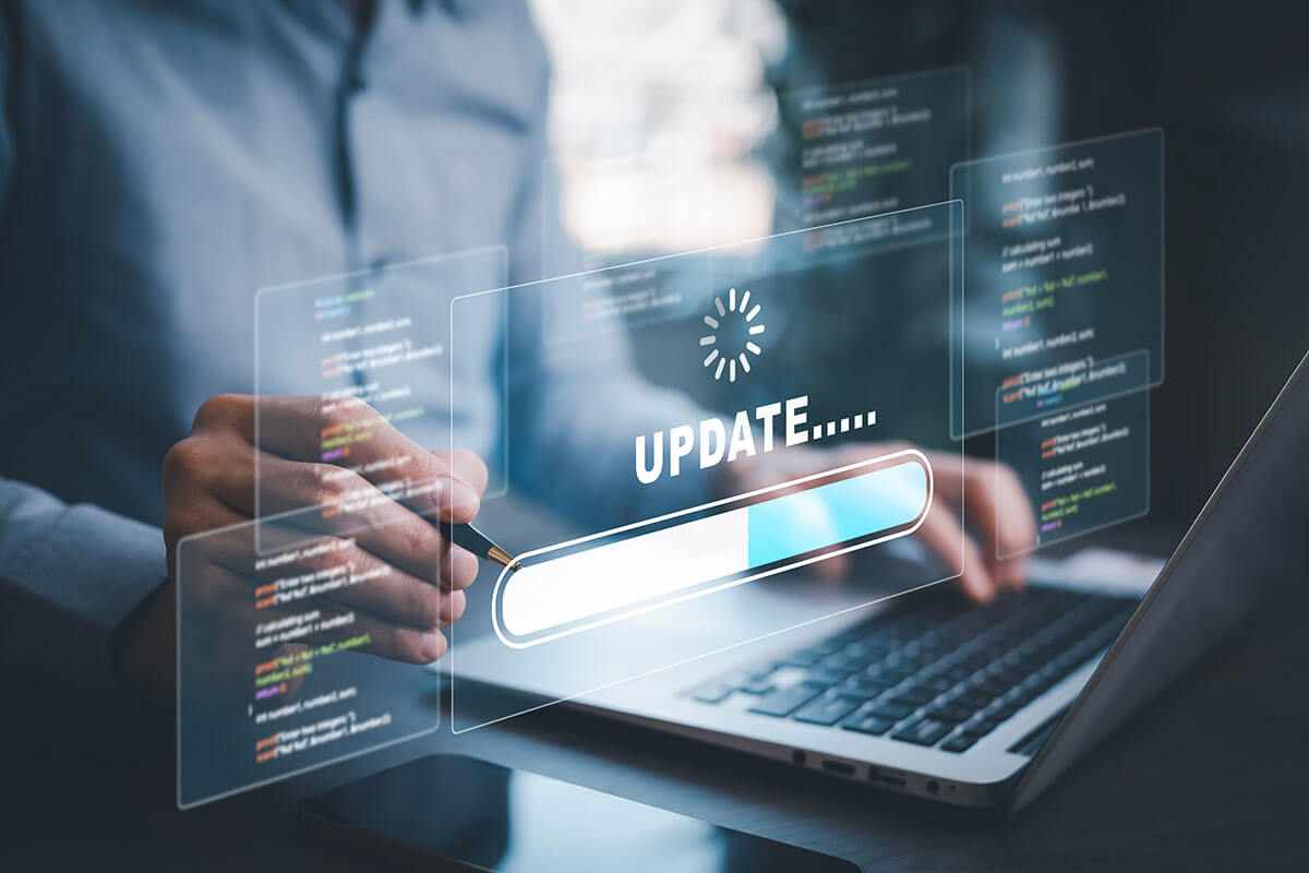 Ein Mensch sitzt vor einem Laptop und hält einen Kugelschreiber in der Hand. Vor ihm ist durchscheinend ein Computer-Update und Programmiercode zu sehen.