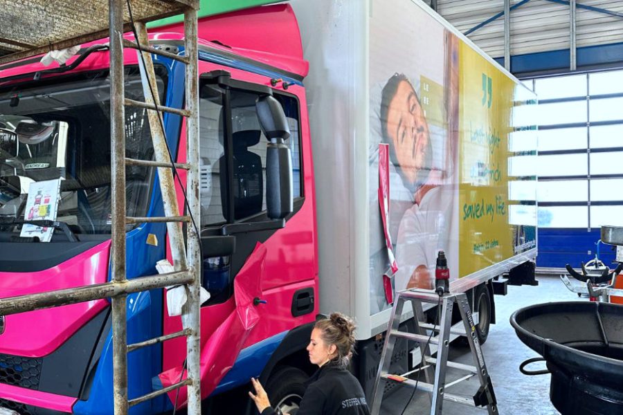 Eine Expertin von STEFFEN MEDIA bringt die pinke Folie am Führerhaus des LKW an.