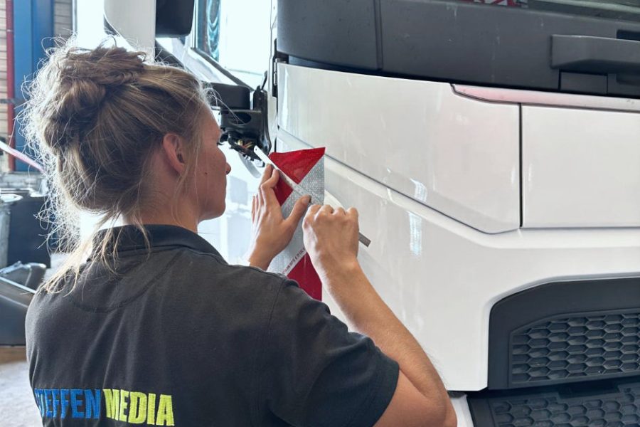 Eine Expertin von STEFFEN MEDIA bringt eine reflektierende Folie am LKW an.